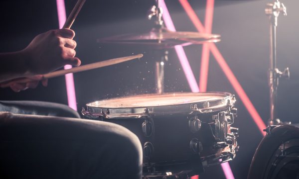 the man plays the drums, the game is on the working drum with sticks close-up. On the background of colored lights. Musical concept with a working drum.