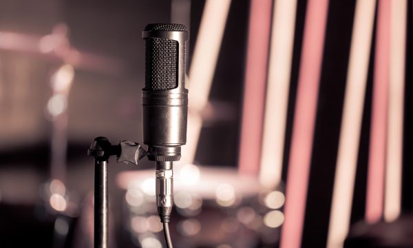 Microphone in recording Studio or concert hall close-up, with drum set on background out of focus. Beautiful blurred background of colored lanterns. Musical concept in vintage style.