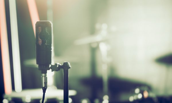 Microphone in recording Studio or concert hall close-up, with drum set on background out of focus. Beautiful blurred background of colored lanterns. Musical concept in vintage style.