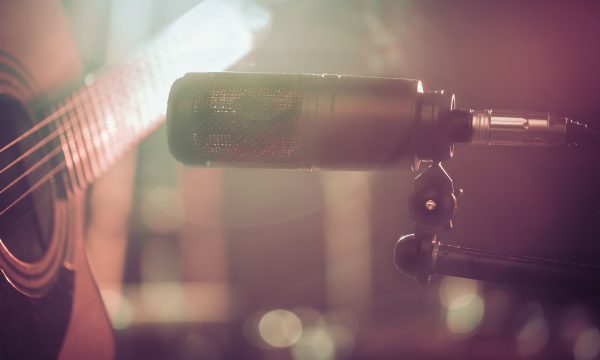 The Studio microphone records an acoustic guitar close-up, in a recording Studio or concert hall, with a drum set on a background in out-of-focus mode. Beautiful blurred background of colored lanterns