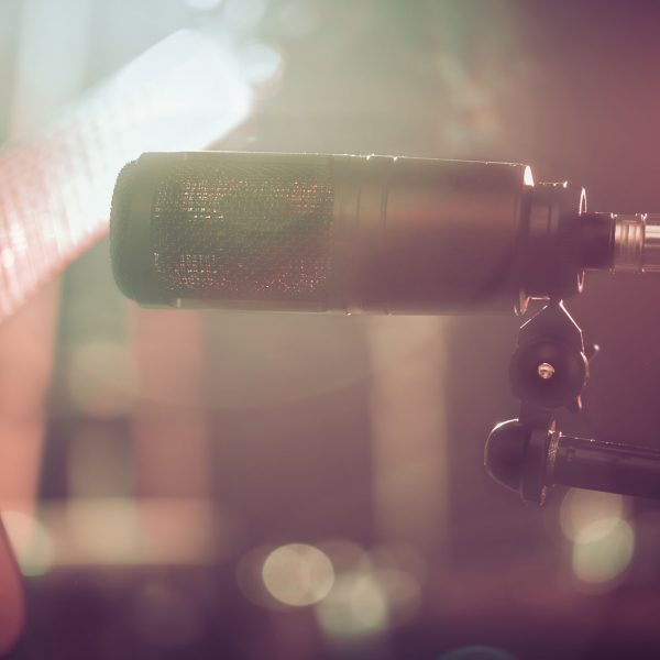 The Studio microphone records an acoustic guitar close-up, in a recording Studio or concert hall, with a drum set on a background in out-of-focus mode. Beautiful blurred background of colored lanterns