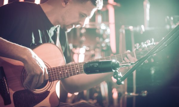 The Studio microphone records an acoustic guitar close-up, in a recording Studio or concert hall, with a drum set on a background in out-of-focus mode. Beautiful blurred background of colored lanterns