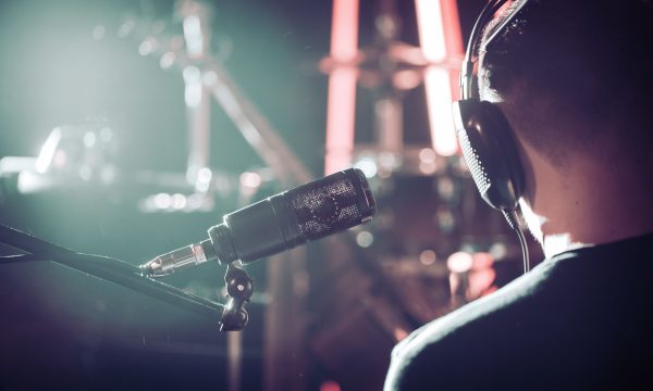 Person with headphones and Studio microphone close-up, in a recording Studio or concert hall, with a drum set on the background in out-of-focus mode. Beautiful blurred background of colored lanterns