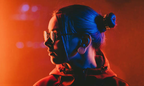 Millennial pretty girl with unusual hairstyle near glowing red neon of city at night. Dyed blue hair in braids. Mysterious hipster teenager in glasses. Reflection of light.