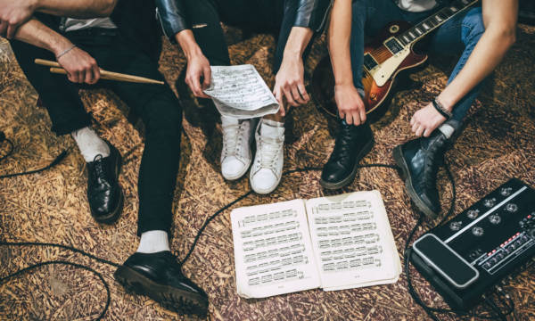 Repetition of rock music band. Cropped image of guitar players and drummer are sitting on the floor at rehearsal base with notes. Top view