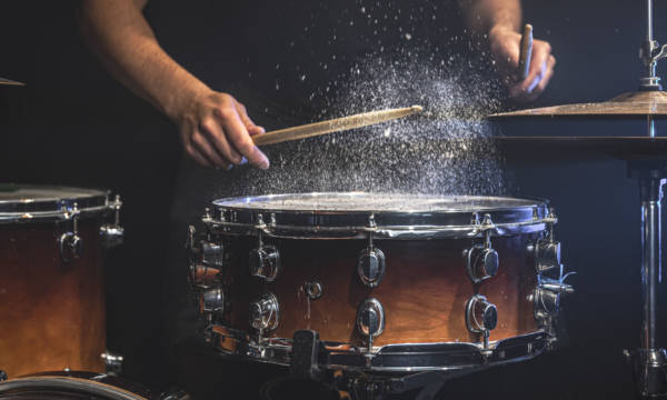 A male drummer plays snare drum with drumsticks in a dark room.