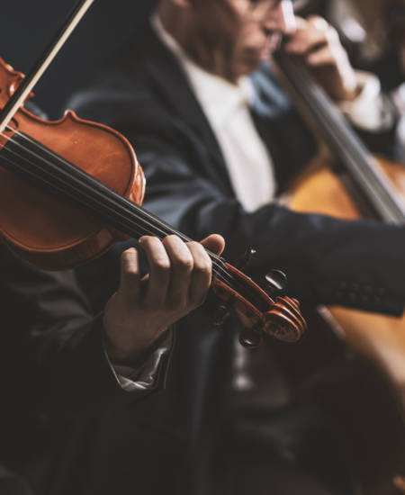 Professional symphonic string orchestra performing on stage and playing a classical music concert, violinist in the foreground