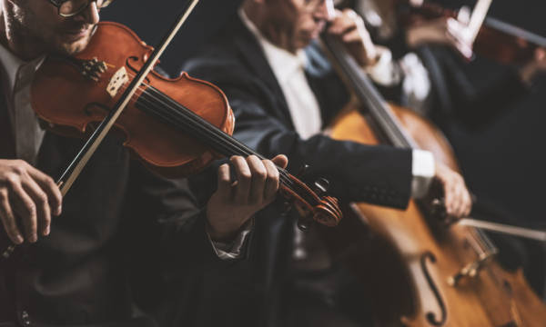 Professional symphonic string orchestra performing on stage and playing a classical music concert, violinist in the foreground