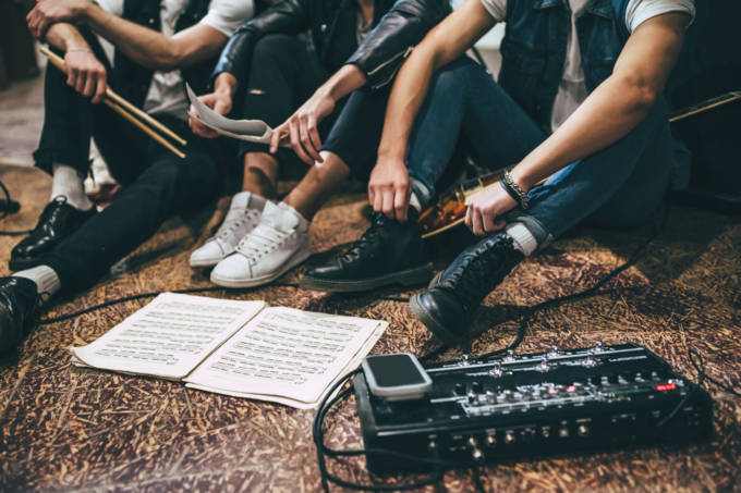 Repetition of rock music band. Cropped image of guitar players and drummer are sitting on the floor at rehearsal base with notes.