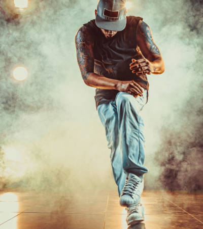 Young cool man break dancing in club with lights and smoke. Tattoo on body.