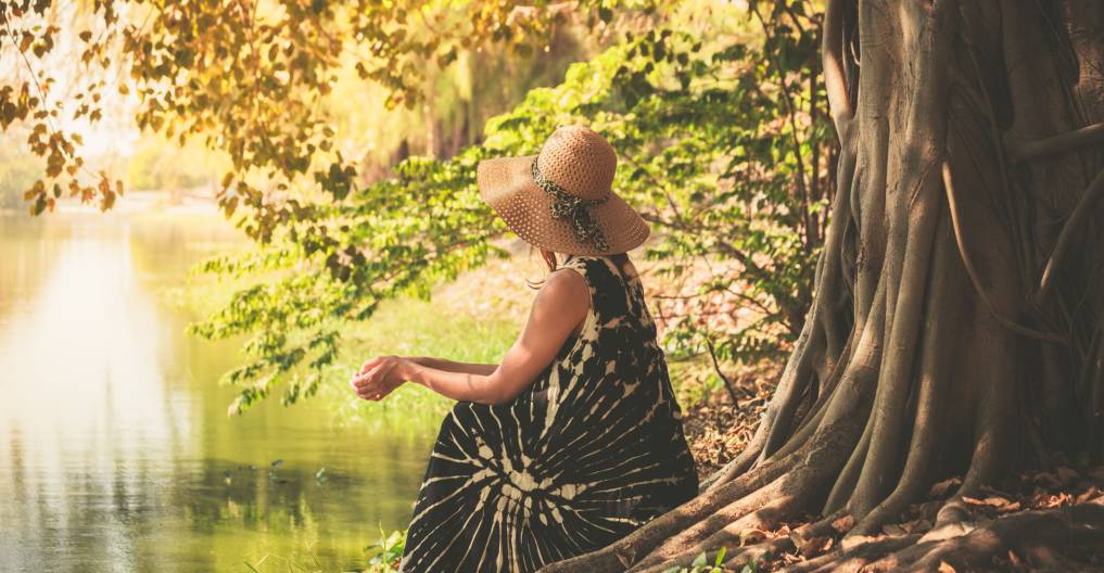 A young woman is sitting under a tree by the river