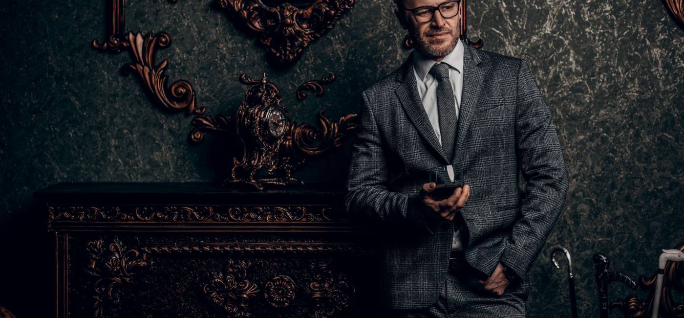 A portrait of a handsome mature man in a formal costume drinking wine. Men's beauty, fashion.