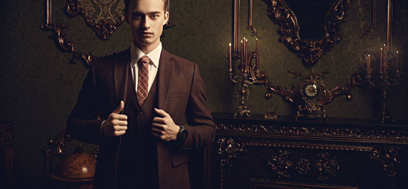 A portrait of a handsome young man in a formal suit posing in a luxury apartments with classic interior. Men's beauty, fashion.