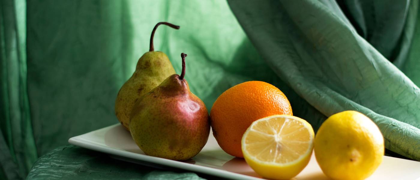 Lemon, orange and pears lie on a white ceramic plate on a table