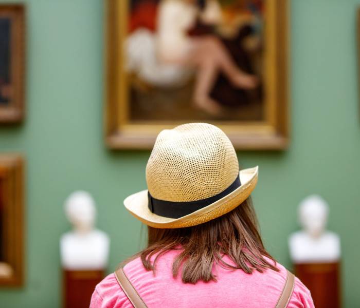 Girl in a hat looks at paintings in a museum