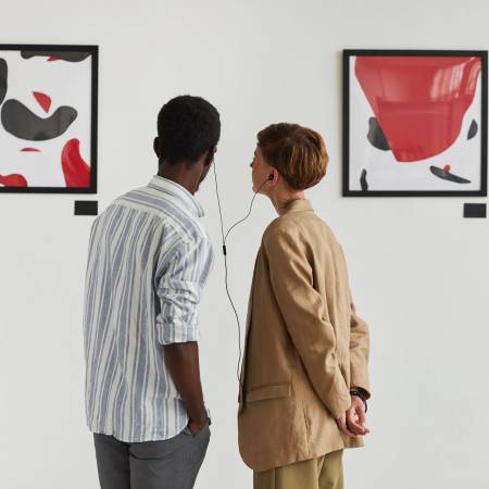 Graphic back view portrait of two young people looking at paintings and sharing audio guide while exploring modern art gallery exhibition, copy space