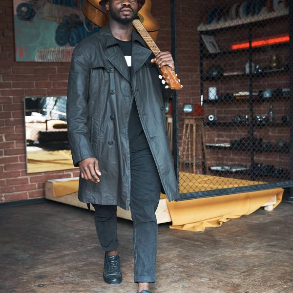 Musician in black trench coat and bucket standing with guitar. Songwriter in loft room. Fashion 2019