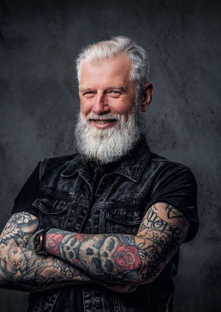 Portrait of glad old man biker dressed in black vest posing with crossed arms.